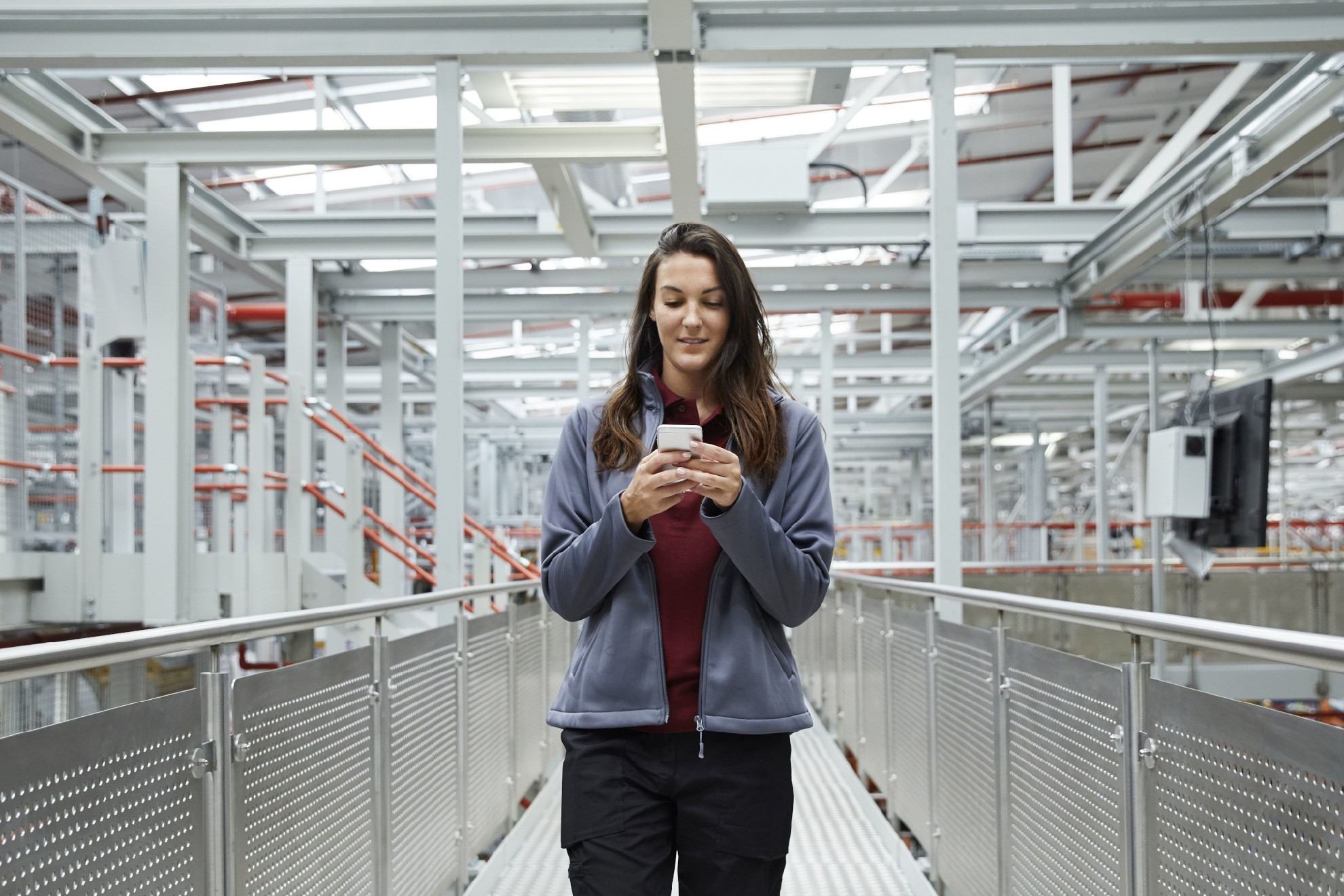 Eine junge Frau in Arbeitskleidung blickt auf ein Smartphone.